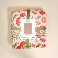 A folded pink floral Everbloom Dusty Rose Snuggle Up Plush Blanket by The Darling Effect, wrapped in green ribbon with a label showing red and green flowers and reading "snuggle up plush blanket.