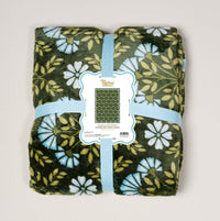 The Darling Effect's Everbloom Forest Green Snuggle Up Plush Blanket features white and blue floral patterns, neatly folded with a light blue ribbon and label—perfect for adding cozy comfort to any space.