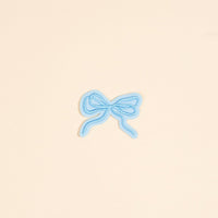 The Darling Effect's Bow Blue Mix & Match Iron-On Patch features a small embroidered light blue bow on a pale beige background—ideal for customizing your style or enhancing other iron-on patches.