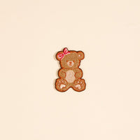The Darling Effect's Teddy Bear Mix & Match Iron-On Patch features a brown teddy bear with a pink bow on a pale background—ideal for customizing jackets or enhancing your colorful patch collection.