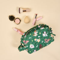 The Darling Effect's Dog Days Essentials Quilted Cosmetic Pouch, featuring a dog print, is displayed on a cream background with makeup brushes, a beauty blender, and lipstick spilling out.
