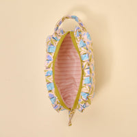 The Darling Effect's Poppin' Petals Aqua Essentials Quilted Cosmetic Pouch features a floral design, yellow zipper, ruffled edges, and pink-striped lining—perfect as a travel pouch against a light beige background.