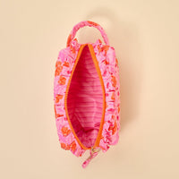 The Darling Effect's Poppin' Petals Hot Pink Essentials Quilted Cosmetic Pouch features pink quilting with orange floral patterns, a top handle, and a light pink striped interior, shown open on a beige background.