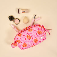 The Darling Effect’s Poppin' Petals Hot Pink Essentials Quilted Cosmetic Pouch, shown with brushes and makeup on a beige background, is a stylish floral bag perfect for organizing beauty essentials on the go.