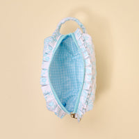 The Darling Effect’s Mrs. Something Blue Essentials Quilted Cosmetic Pouch features a white quilted exterior with blue floral print and ruffled trim, and opens to reveal a blue and white checkered interior.