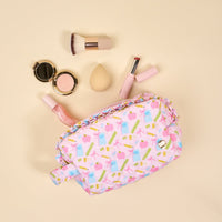 The Darling Effect's School's In Session Essentials Quilted Cosmetic Pouch, featuring gift and lipstick designs, sits open to reveal makeup must-haves—brush, blush compact, sponge, lipstick, and gloss—against a beige background.