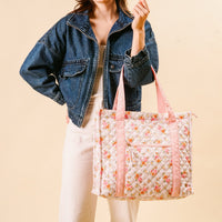 A woman in a denim jacket and light dress holds the-darling-effect's Endless Daydream Cream The Everyday Quilted Tote Bag with floral print and pink handles, posing against a beige background.