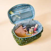 The Darling Effect’s Everbloom Forest Green Glam & Go Quilted Cosmetic Bag is open, displaying a comb, makeup brushes, tubes of makeup, and an eyelash curler—ideal as a chic travel toiletry bag.