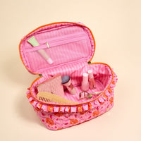 The Darling Effect's Poppin' Petals Hot Pink Glam & Go Quilted Cosmetic Bag, trimmed in orange, opens to reveal must-have makeup essentials—perfect as a stylish travel bag for your beauty accessories.