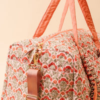 The Darling Effect Everbloom Dusty Rose On-the-Go Quilted Weekender Bag features pink handles, a floral red and green pattern, a gold zipper, and a detachable, adjustable pink shoulder strap.