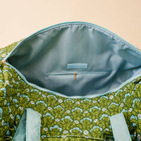 The Darling Effect Everbloom Forest Green On-the-Go Quilted Weekender Bag features a floral print, light blue zipper, striped blue lining, inner zip pocket, and an adjustable strap—ideal for travel and comfort on the go.