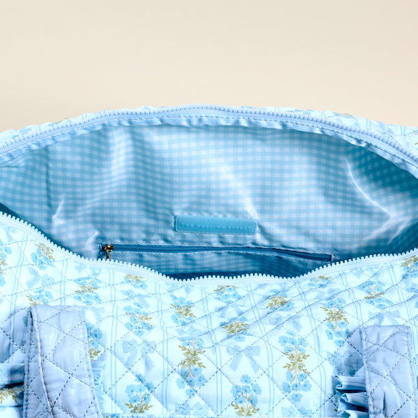 A close-up of The Darling Effect's Oh So Fancy Blue On-the-Go Quilted Weekender Bag features a floral pattern, blue and white checkered lining, and inner zippered pocket—spacious for everyday use or short getaways.