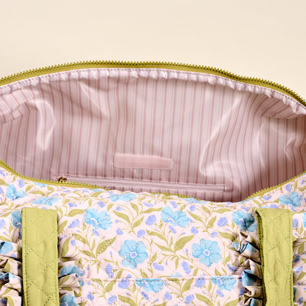 The Darling Effect’s Poppin' Petals Aqua On-the-Go Quilted Weekender Bag features a pale pink background, blue florals, green trim, and a pink satin striped lining with a zip pocket—ideal for short trips or getaways.