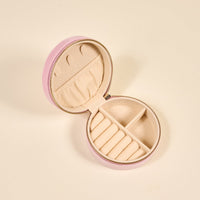 The Darling Effect’s Bow Pink Round Velvet Jewelry Case is open, showing a beige interior with ring slots and a zippered compartment for accessories.