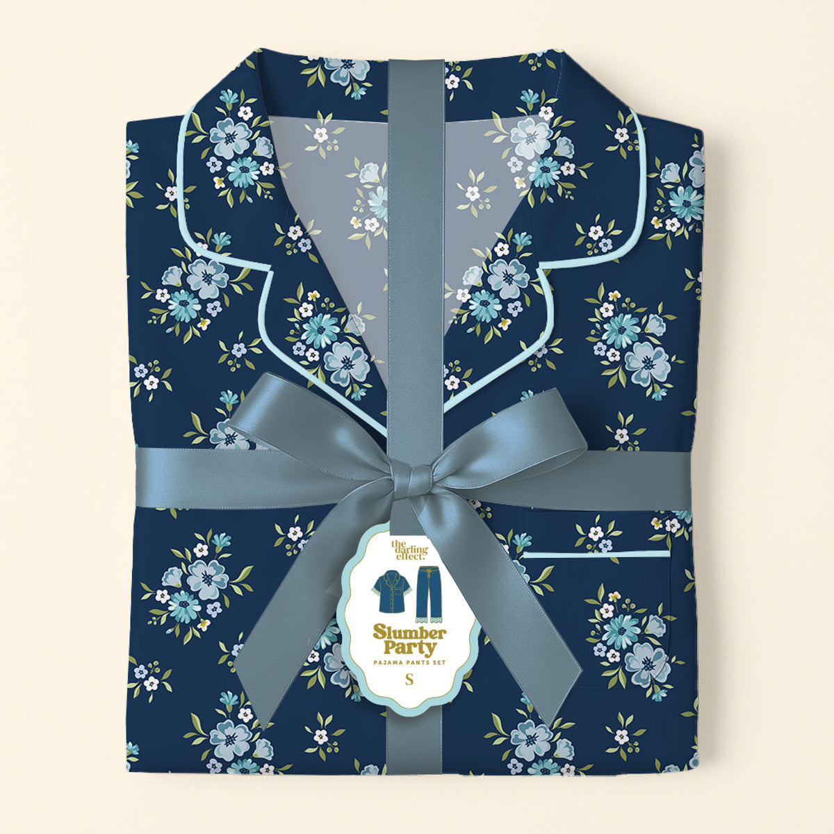 Folded Endless Daydream Navy Slumber Party Pajama Pants Set by The Darling Effect, featuring a light blue and white floral print on ultra-soft fabric, tied with a satin ribbon. Tag displays product name and a relaxed fit illustration.