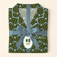 A folded Everbloom Forest Green Slumber Party Pajama Pants Set by The Darling Effect, in soft fabric with a floral print, is tied with a blue ribbon and bow. A tag shows the product name and a pajamas illustration.