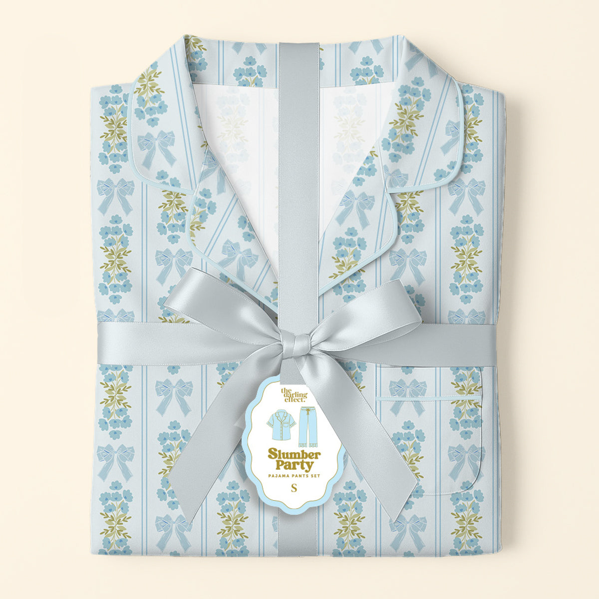 Folded Oh So Fancy Blue Slumber Party Pajama Pants Set by The Darling Effect, featuring a floral and bow design on ultra-soft fabric, tied with a satin ribbon and a “Slumber Party Pajama Party Kit” tag on a soft cream background.