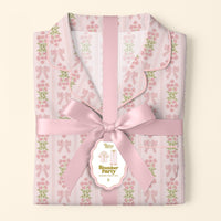 Folded Oh So Fancy Pink Slumber Party Pajama Pants Set by The Darling Effect, featuring a floral and bow pattern in ultra-soft fabric, tied with a pink satin ribbon and gift tag labeled "Slumber Party Pajama Set, S," on a light background.