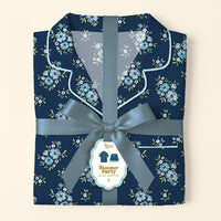 The Darling Effect’s Endless Daydream Navy Slumber Party Pajama Shorts Set features folded, ultra-soft navy pajamas with a light blue floral pattern, tied with a satin ribbon and bow. Gift-ready, it includes a tag with an illustration of the set.
