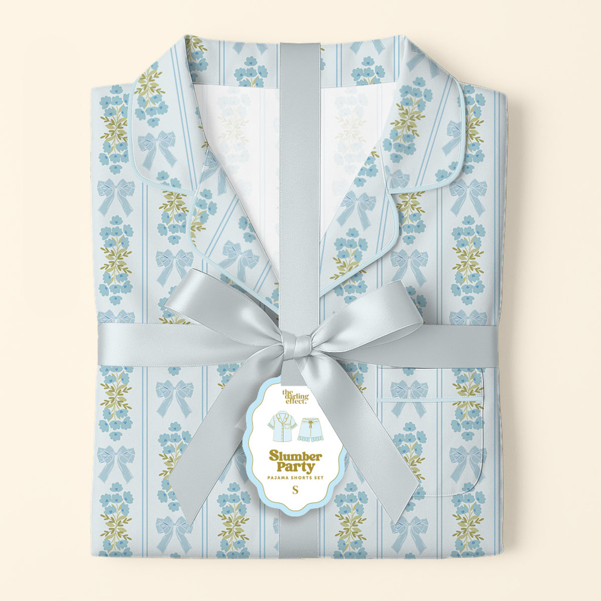 Folded Oh So Fancy Blue Slumber Party Pajama Shorts Set by The Darling Effect features a collared, ultra-soft top and shorts, wrapped in silver satin ribbon with a tag and playful illustrations of the relaxed fit.