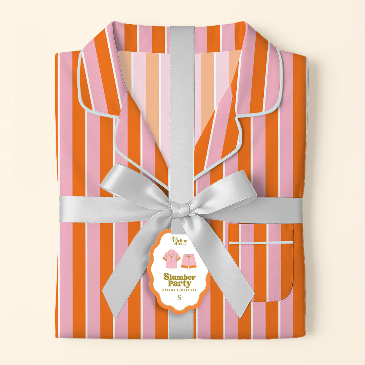 Folded Sicily Stripes Pink Slumber Party Pajama Shorts Set by The Darling Effect, featuring pink, orange, and red stripes, silver ribbon and tag, ultra-soft fabric, white piping on collar and edges for a relaxed fit.