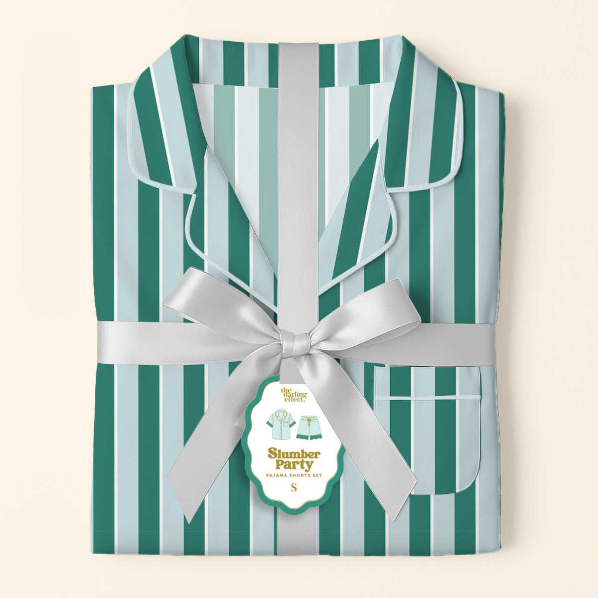 The Darling Effect’s Sicily Stripes Teal Slumber Party Pajama Shorts Set, in ultra-soft fabric with teal and light blue stripes, is folded and tied with a silver ribbon, featuring a gift tag showing a small pajamas illustration and "S" for size.