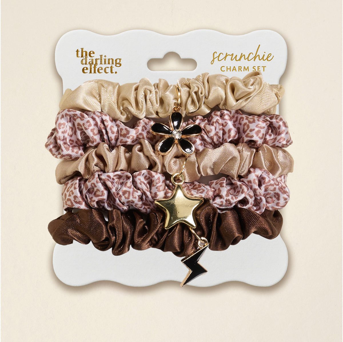 The Darling Effect's Born Wild Scrunchie Charm Set features leopard, gold, and brown scrunchies adorned with flower, star, and lightning bolt hair charms for a chic accessory upgrade.