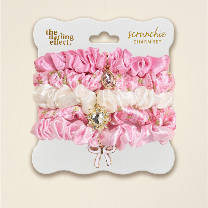 Three pink and white satin scrunchies with floral patterns, each featuring a dangling jeweled hair charm, are beautifully presented on a decorative card labeled “Oh So Fancy Pink Scrunchie Charm Set” by The Darling Effect—an ideal pick for anyone looking for stylish hair accessories.