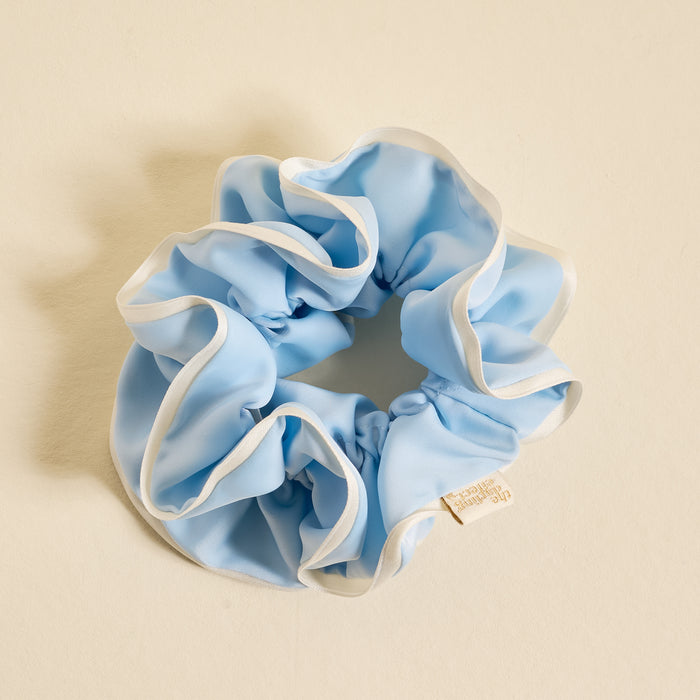 The Darling Effect Light Blue Ruffle Up Scrunchie features a voluminous, oversized design with white trim edges, gentle hold, and a small branded label—shown on a cream background.