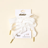 Frilly White Step It Up Shoelaces by The Darling Effect—white, durable laces with gold aglets—attached to a branded card reading "shoelaces" and "ACCESSORIZE YOUR SHOES," displayed on a light beige background.