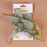 Gingham Green Step It Up Shoelaces by The Darling Effect feature green and white gingham with gold tips, tied in bows and displayed on a branded card. Durable laces to stylishly accessorize your shoes.