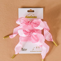 A pair of pink and white gingham durable shoelaces with gold tips, styled in bows and displayed on a branded card reading Step it up shoelaces from The Darling Effect, set against a tan background.