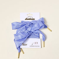 Gingham Royal Blue Step It Up Shoelaces by The Darling Effect feature blue and white gingham with gold tips, tied in bows, and come on branded packaging. Add a stylish, durable touch to your shoes with these chic shoelaces.