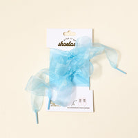 A pair of Sheer Blue Step It Up Shoelaces by The Darling Effect, tied in bows on a white card labeled "shoelaces" and "ACCESSORIZE YOUR SHOES," are displayed against a cream background.