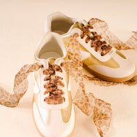 Sheer Cheetah Step It Up Shoelaces by The Darling Effect add bold flair to gold and white sneakers, combining style and personality with every step.