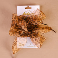 A large, sheer cheetah-print hair bow is attached to a white card labeled "The Darling Effect" and "Sheer Cheetah Step It Up Shoelaces," shown against a neutral beige background—perfect for pairing with durable shoelaces.
