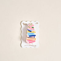 The Darling Effect's Book Nook Shape Up Claw Clip is a clear acrylic hair accessory shaped like stacked colorful books with pink flowers and green leaves, presented on a white backing card.