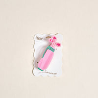 The Golf Clubs Shape Up Claw Clip by The Darling Effect is a pink golf bag-shaped hair accessory with clubs, perfect for cute hairstyles. Comes on a white card that says "The Cutting Effect" and "Hold your hair back in style.