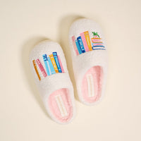 Book Nook Fuzzy Slippers by The Darling Effect: cozy white plush slippers embroidered with vibrant stacks of books and a potted plant.