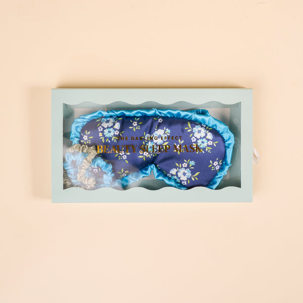 The Darling Effect's Endless Daydream Navy Beauty Sleep Mask set includes a navy floral mask and two satin scrunchies, all elegantly packaged in a light blue gift box.