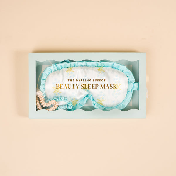 The Darling Effect Oh So Fancy Blue Beauty Sleep Mask gift box features a floral satin sleep mask with ruffled trim and two mini satin scrunchies in blue and nude shades.