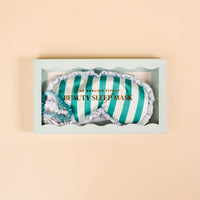 The Darling Effect Sicily Stripes Teal Beauty Sleep Mask features soft teal and white stripes with ruffled edges, displayed in a mint green box—ideal to pair with your favorite satin scrunchies or sleep set.