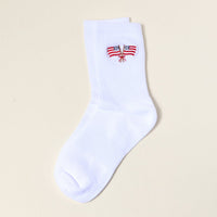 The Darling Effect’s American Flags Embroidered Crew Socks feature a single white sock adorned with a delicate design of two crossed American flags tied with a red ribbon at the ankle. Displayed on a simple light background, this elegant women’s sock offers a subtle, patriotic touch to your collection.