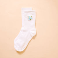 The Darling Effect’s Floral Blue Embroidered Crew Socks feature white ribbed fabric with a blue floral embroidery and green leaves—stylish socks that add a charming touch to any collection.