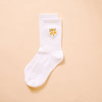 The Darling Effect Floral Yellow Embroidered Crew Socks feature a small yellow flower with green leaves on white fabric, shown on a light beige background. Available in women's sizes 5–10.