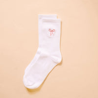Pink Bow Embroidered Crew Socks by The Darling Effect—women's white socks with a small pink bow near the top, shown on a light beige background.