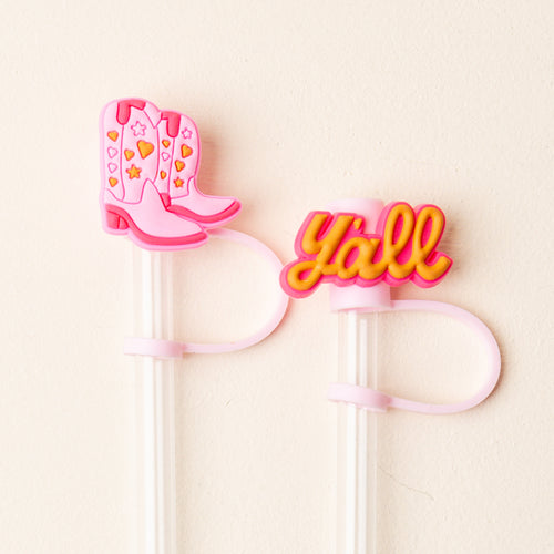 The Darling Effect's Classic Cowgirl Straw Topper Set includes two clear reusable straws with silicone toppers: pink cowboy boots with hearts and stars, and a "y'all" design in yellow and pink—fun accessories to add personality to any drink.