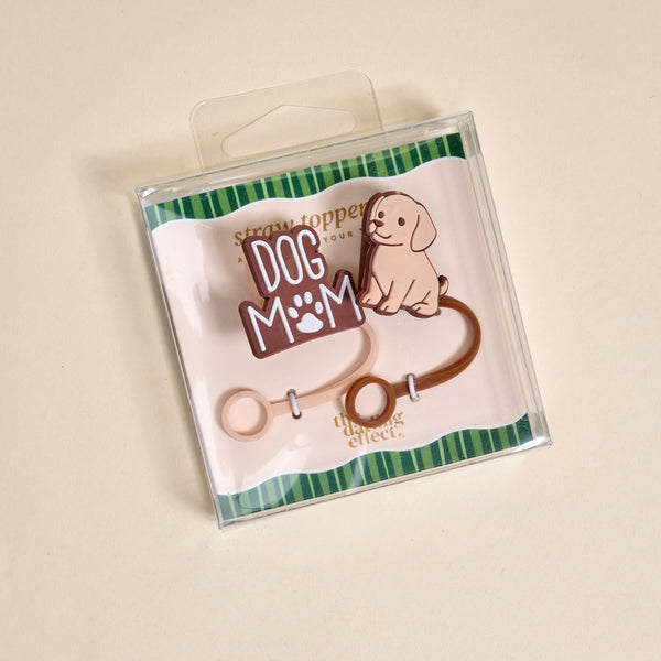 The Darling Effect Dog Mom Straw Topper Set includes two silicone toppers: one with "DOG MOM" and a paw print, and one shaped like a smiling cartoon dog. Both come on a striped green and white background.