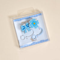 The Darling Effect's Oh So Fancy Blue Straw Topper Set includes two blue silicone toppers—a bow and a flower—packaged in a clear box with striped background, making your drinkware leak-resistant and stylish.