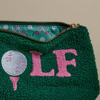 The Darling Effect’s Golf Teddy Pouch is a green textured zip pouch with stitched golf ball, tee, and pink "LF" details. Inside, its lining features playful golf clubs and balls on a light blue background—perfect as a stylish organizer.